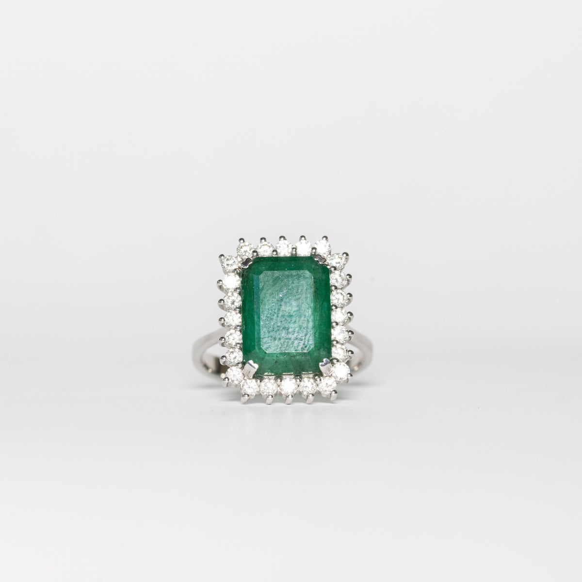 18kt white gold ring with central emerald cut emerald and diamond surround