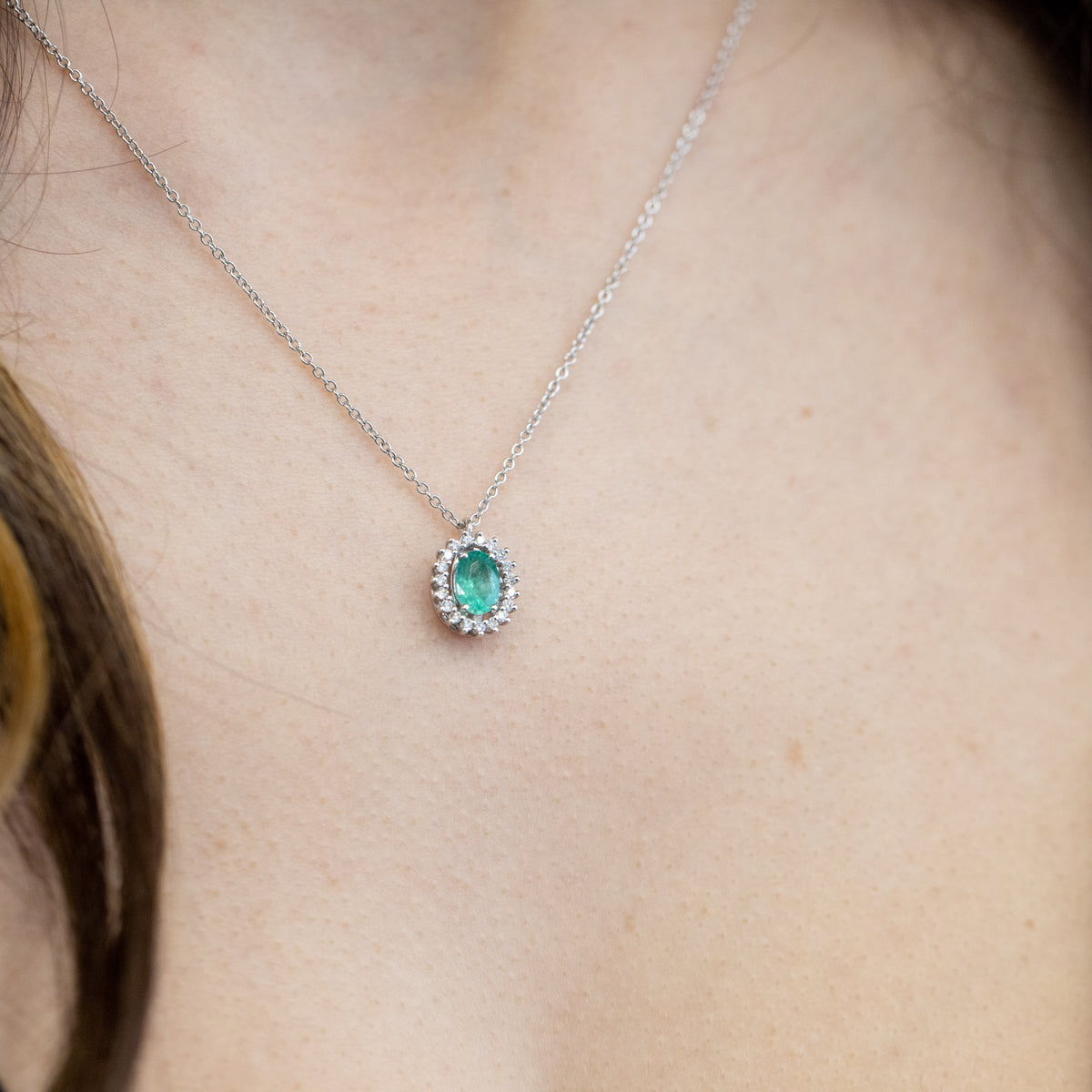 18kt white gold necklace with central emerald surrounded by diamonds. Fancy setting