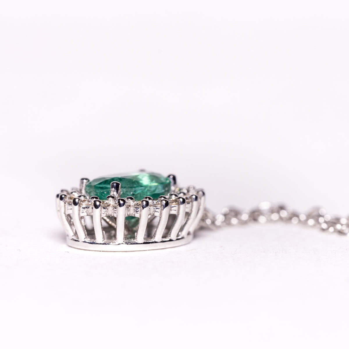 18kt white gold necklace with central emerald surrounded by diamonds. Fancy setting